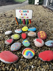 The CAMHS rock garden with 15 colourfully painted rocks and a sign saying CAMHS rock garden.