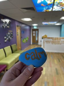 A painted rock in the CAMHS waiting area. The rock is blue with the word calm painted in orange.