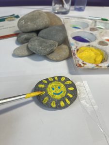 A painted rock in the CAMHS waiting area. The rock has a smiley sun painted in yellow.