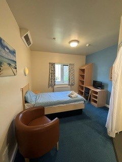 A patient's bedroom with bed, chair and shelves