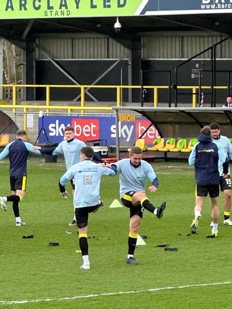 Harrogate Town AFC players warming up on the pitch wearing North Yorkshire Talking Therapies branded t-shirts