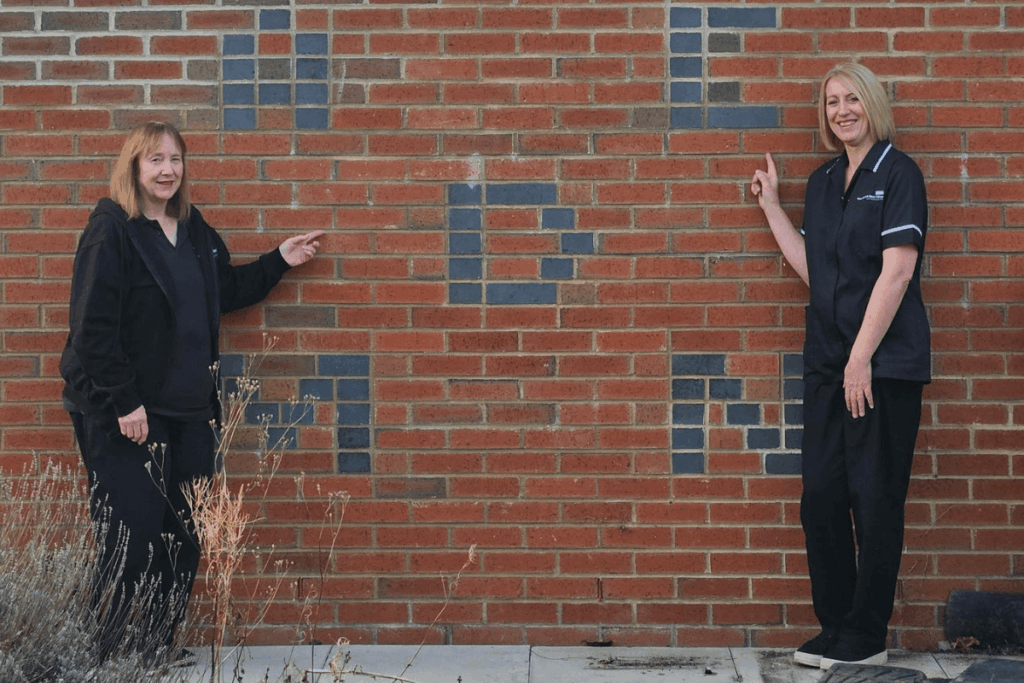 Karen and Angela pointing at initials in brickwork