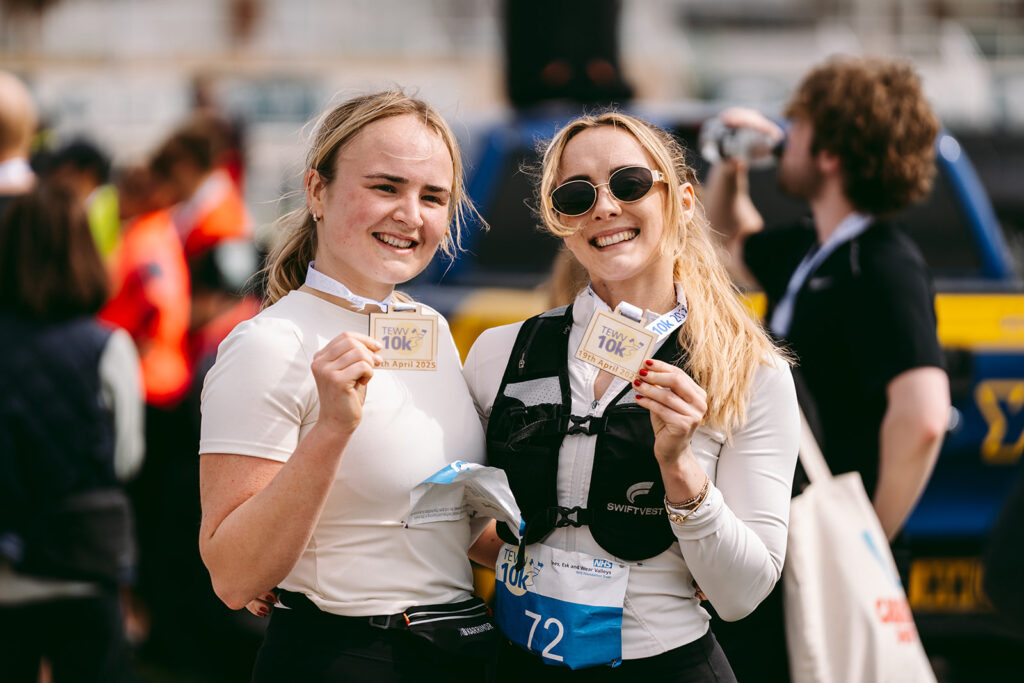 A photo of two women smiling at the camera. They both have wooden TEWV 10k medals around their neck.