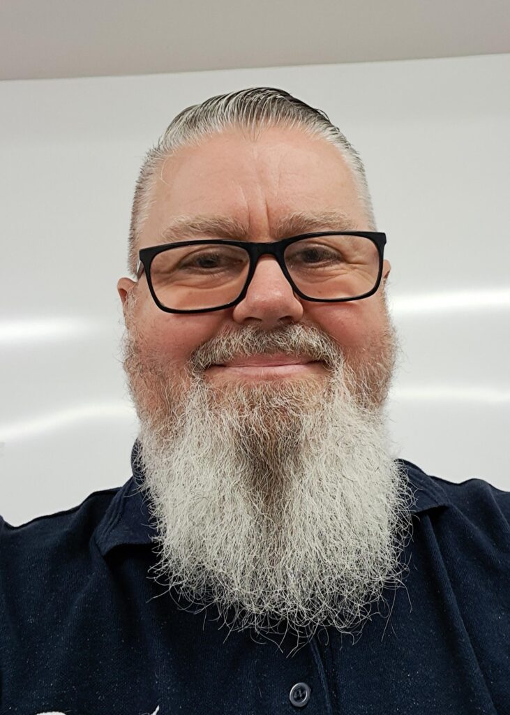 Man with grey hair and beard wearing glasses and smiling