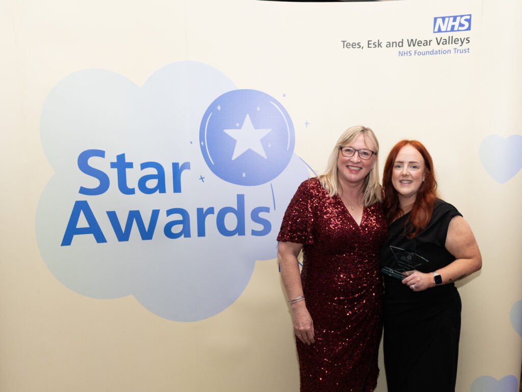 Excellence in learning winner Hayley Hawksby smiling with a star shaped trophy. She is standing in front of a yellow Star Awards banner. He is standing with Lisa Taylor, director of operations at Tees, Esk and Wear Valley NHS Foundation Trust.
