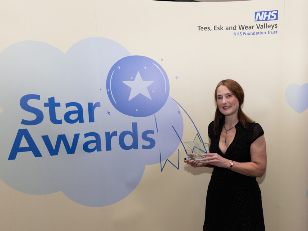 The mum of Emily Norton stands with a star shaped trophy in front of the yellow Star Awards banner.
