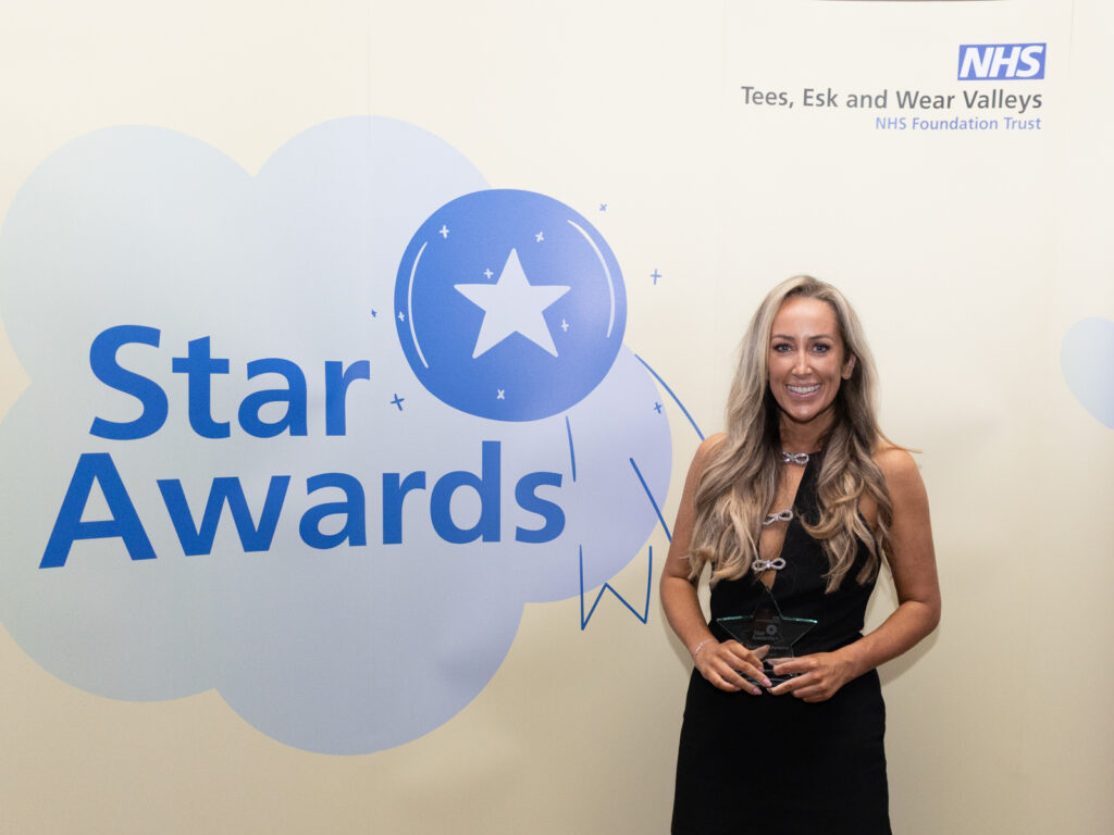 Cocreation champion winner Ruth Lord smiling with a star shaped trophy. She is standing in front of a yellow Star Awards banner.