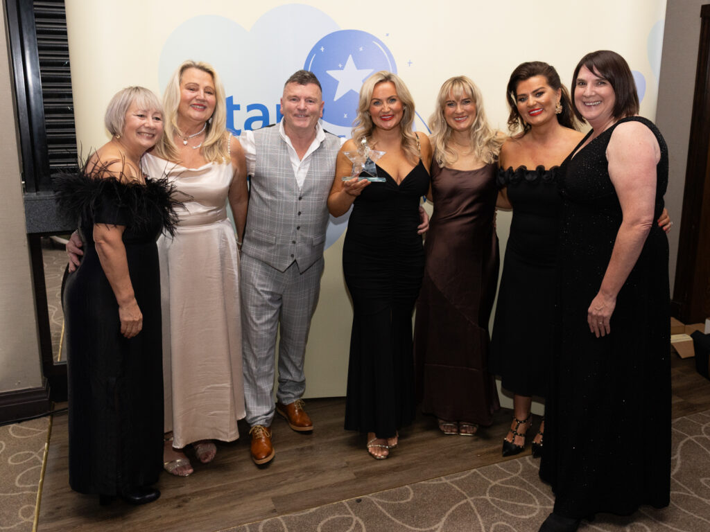 Co-creation in action winner Chris's Voice. The family - Rachel, Anna, Nicola, Trish and Mick, are standing with a star shaped trophy. They are standing in front of a yellow Star Awards banner. They are with chief nurse Beverley Murphy.