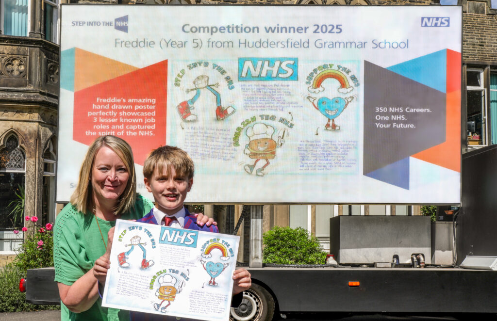 young boy and his female teacher stood holding his original artwork in front of a large digital version of his advert on a big truck.