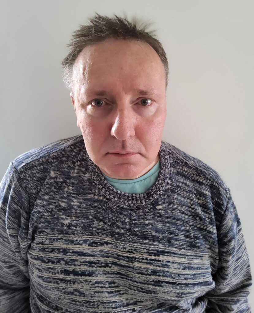 Man with brown hair wearing a grey and white jumper