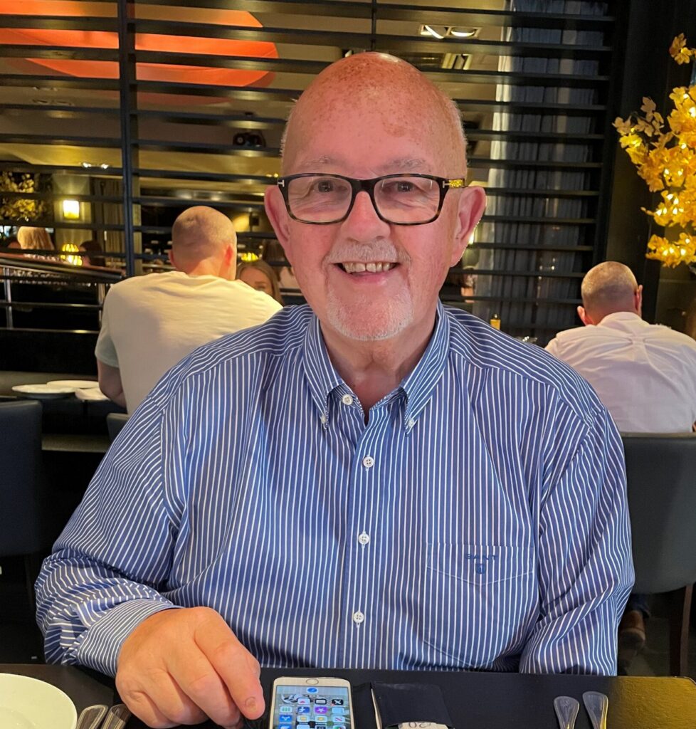 Man with a bald head and glasses smiling, wearing a blue and white striped shirt