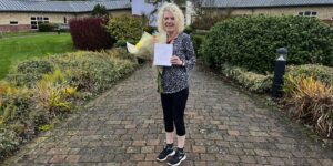 Mary in West Park Hospital gardens with flowers and a card to celebrate 10 years as a volunteer