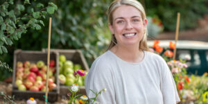 Steph Smith wearing a white top, surrounded by apples and flowers, smiling into the camera